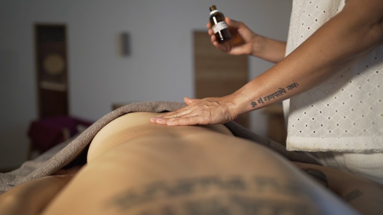 A therapist applying oil to the back of a person during a massage session in a serene setting.